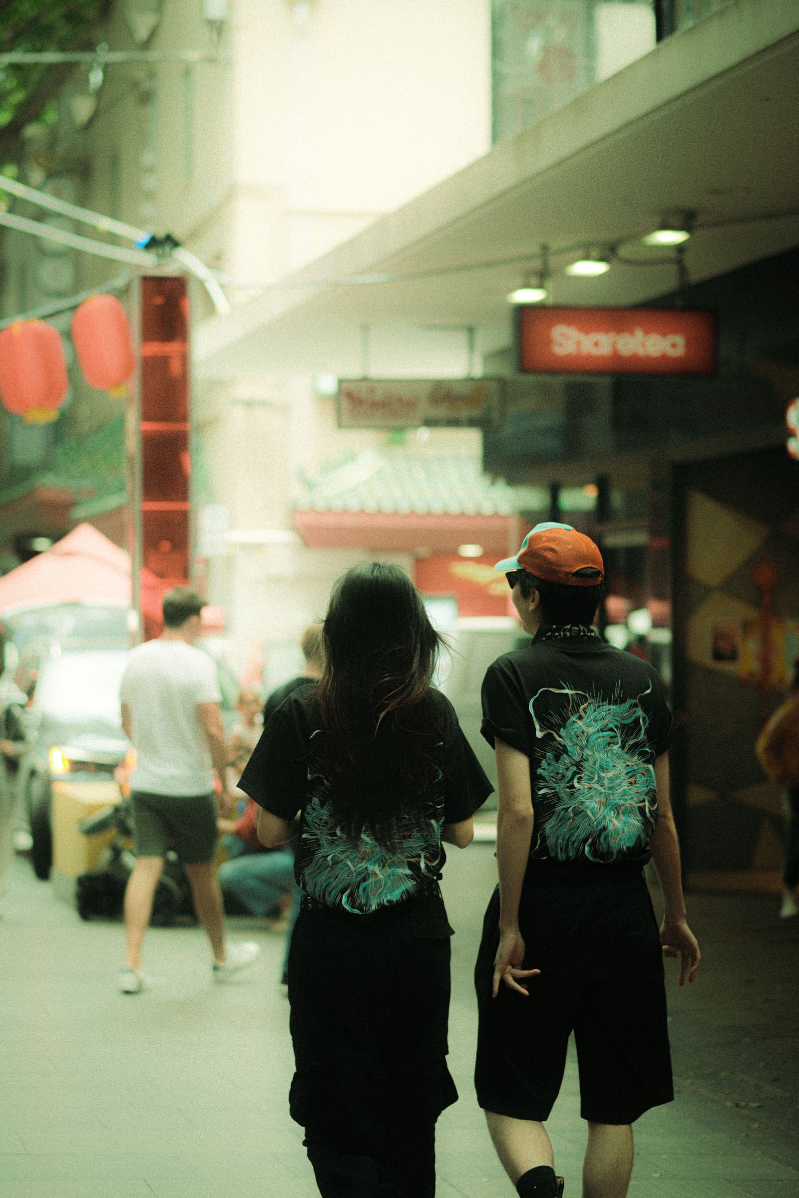 Two models walking away down a lantern-lit street, the back prints showing