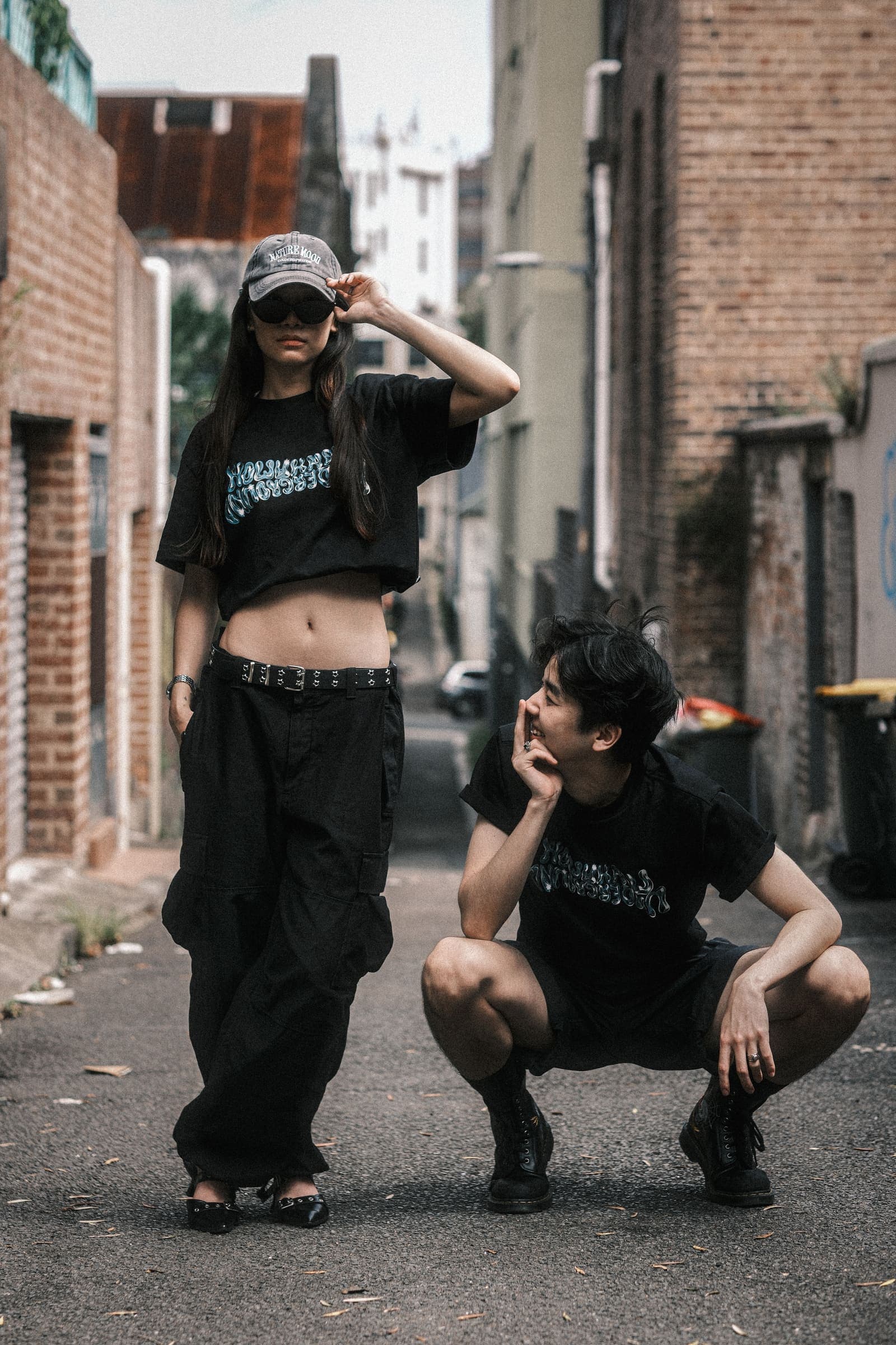 Two models in a laneway, one standing and one crouching